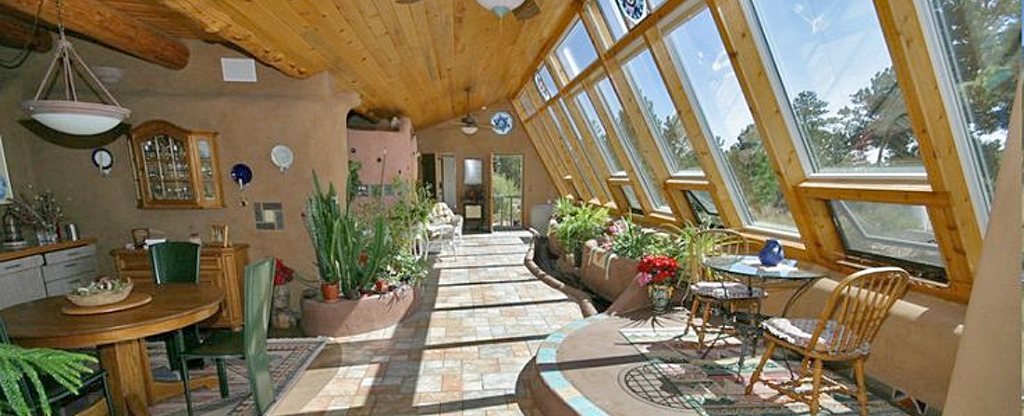 Earthship interior living space with natural light, botanical cells, and earthy finishes